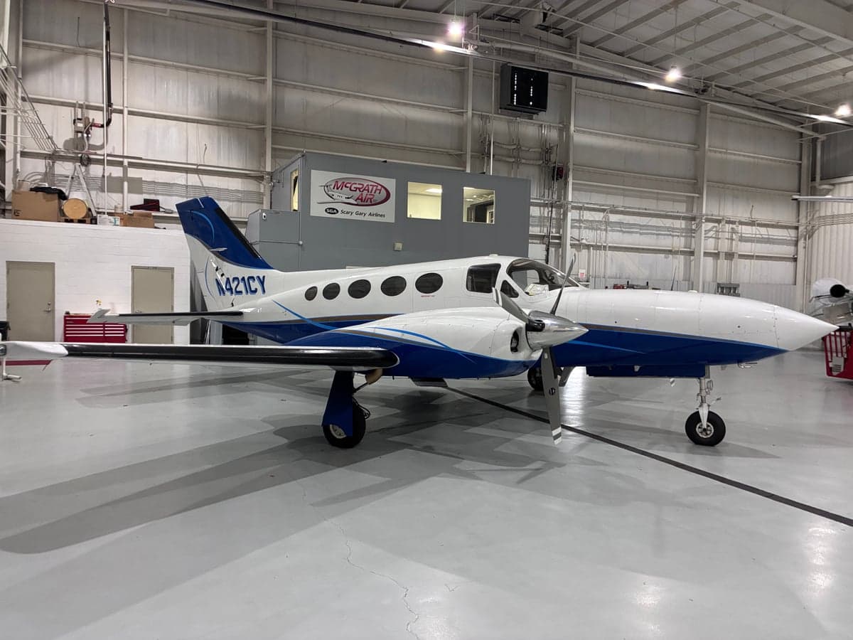 A white and blue Cessna 421CY sits inside a hangar.