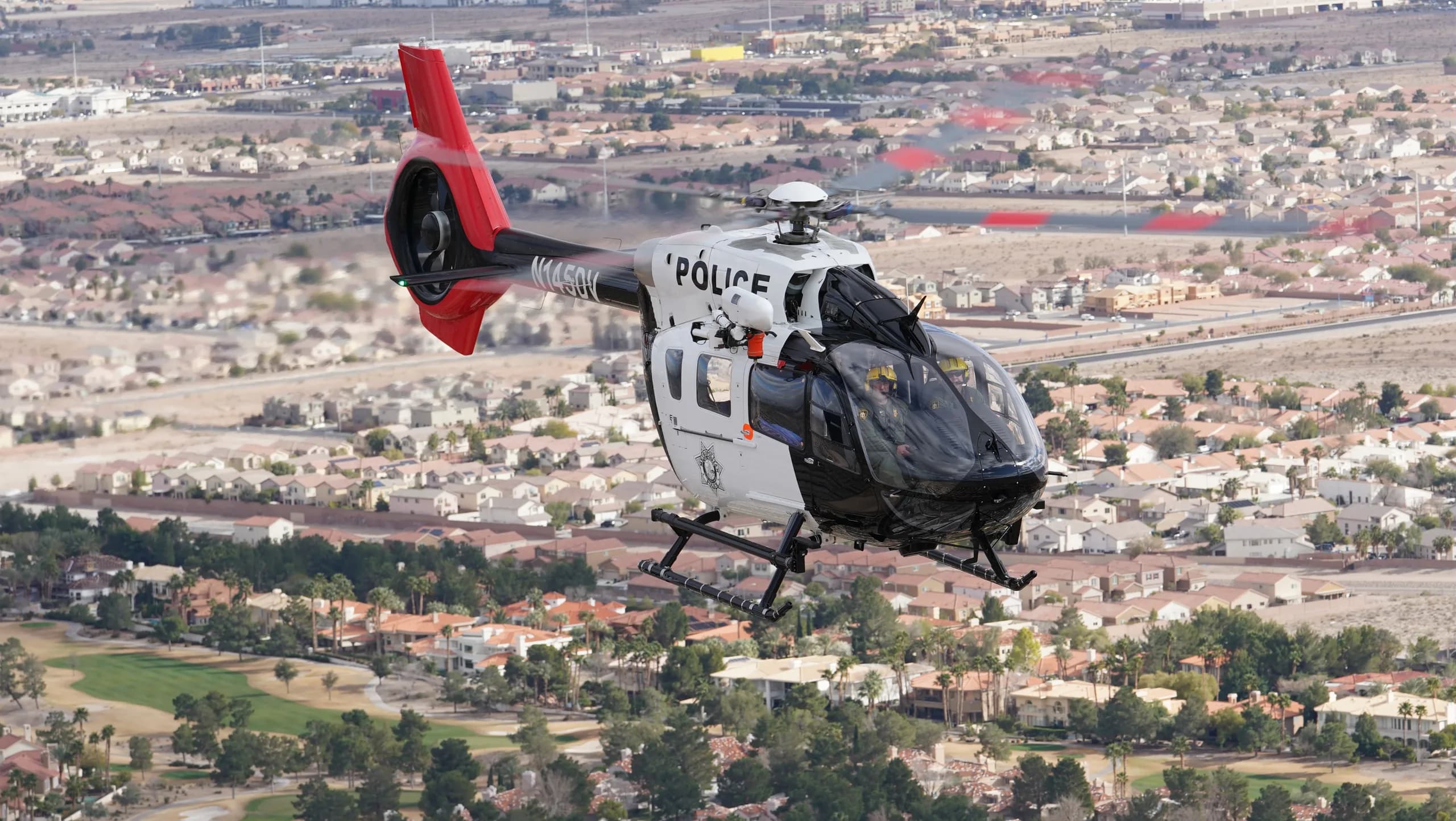 A black and white police helicopter flying over a suburban area.
