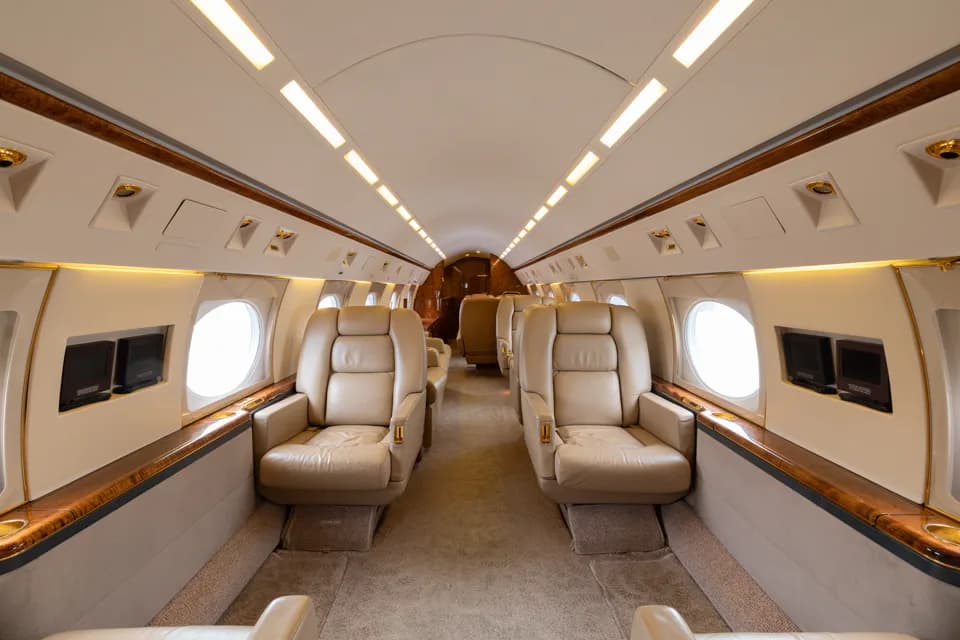 The luxurious interior cabin of a business jet with beige leather seats and polished wood trim.