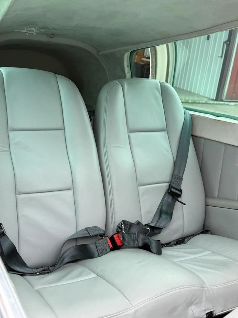 Two light gray leather passenger seats with seatbelts in the cabin of a small aircraft.