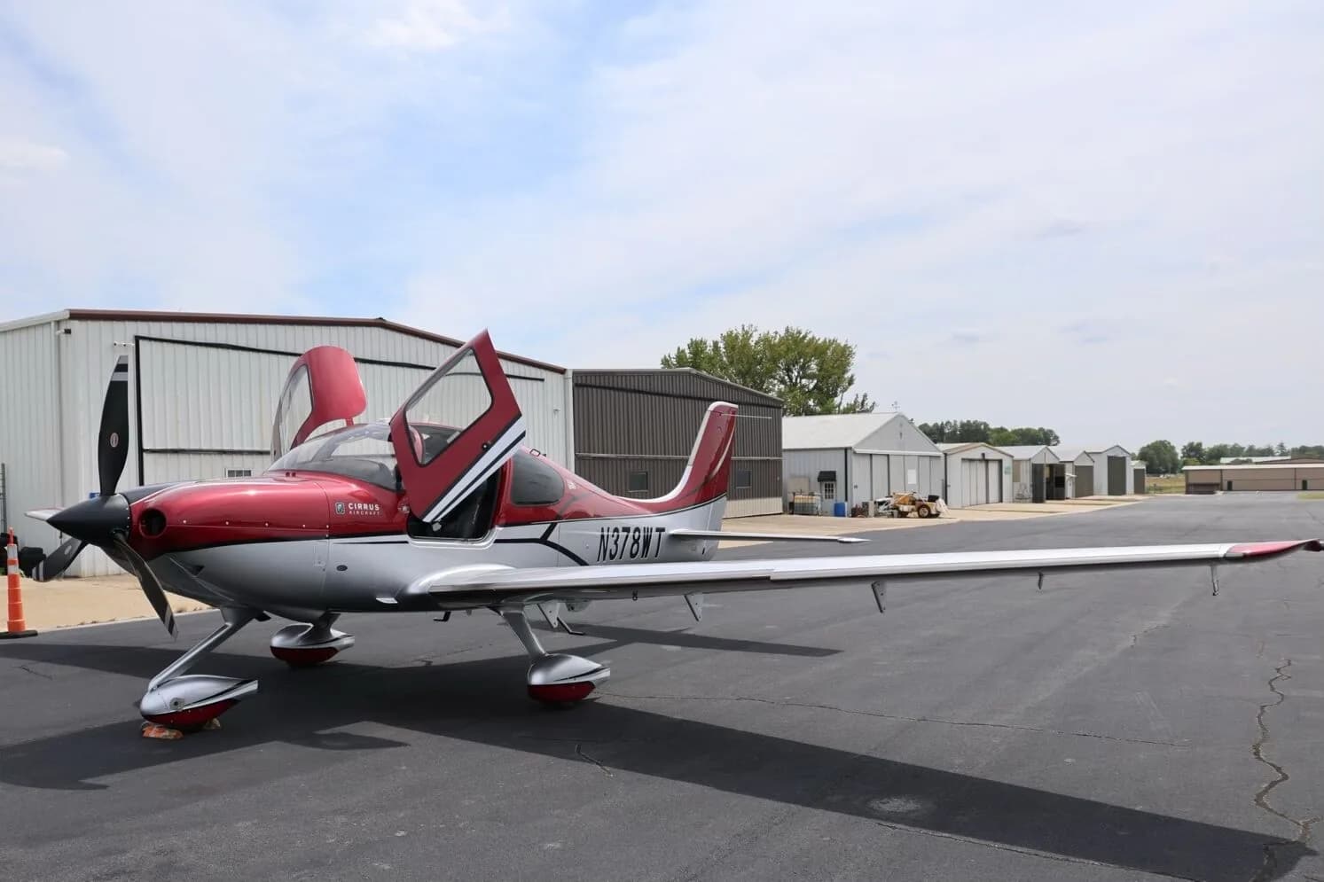 A red and silver Cirrus SR22T aircraft, N378WT, with its doors open, parked on an airfield tarmac.