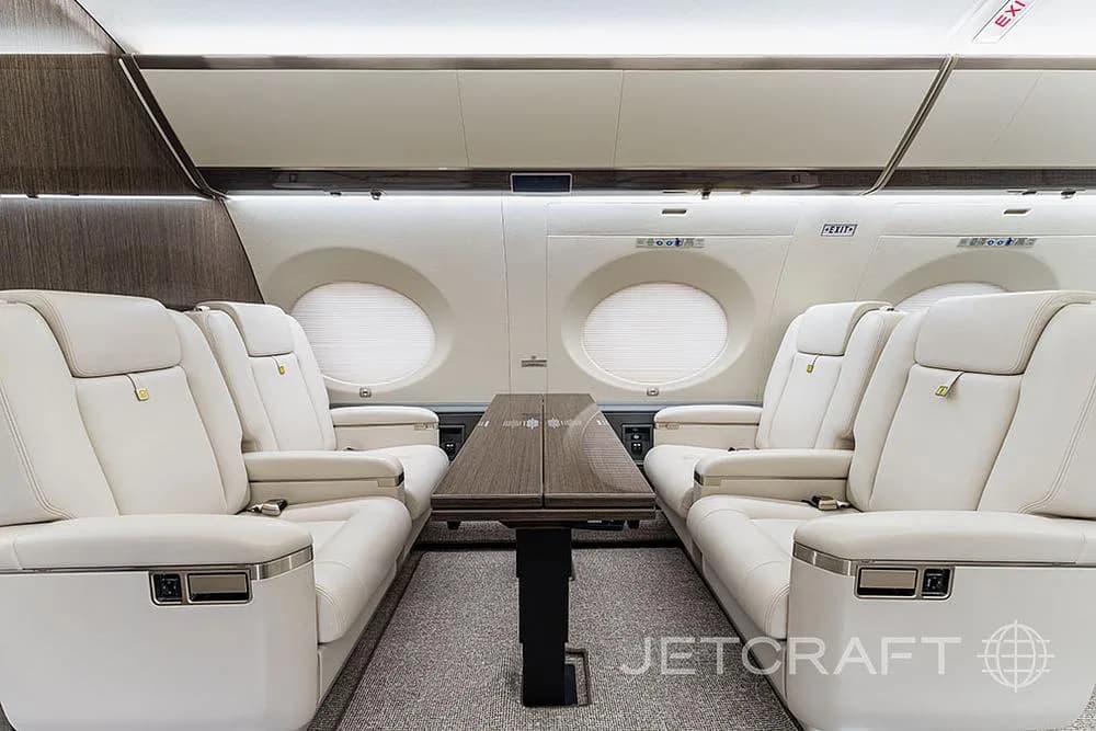 A close-up view of two sets of cream leather seats facing each other across a dark wood table in a private jet cabin.