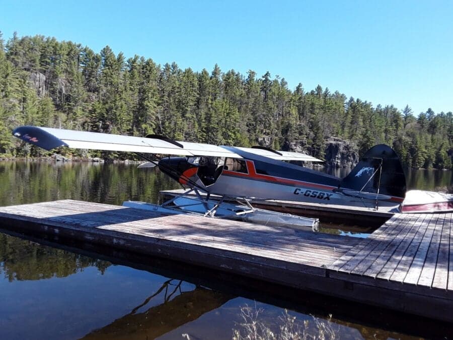 A black, gray, and orange Super Cub on floats is docked on a lake.