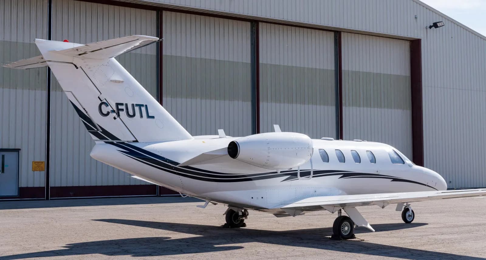 A white Cessna Citation CJ3 is parked in front of a hangar.