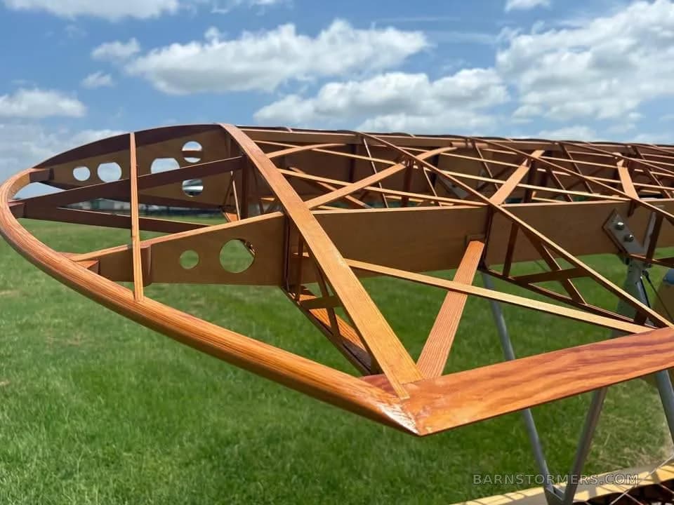 A close-up view of the intricate wooden rib and spar structure of a biplane wing against a blue sky.