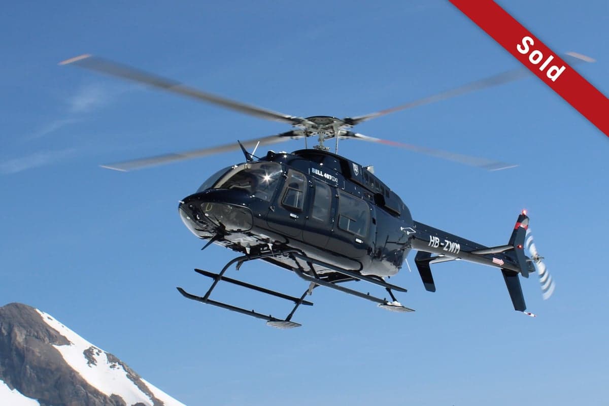 A black Bell 407GX helicopter, registration HB-ZWM, in flight with a SOLD banner.