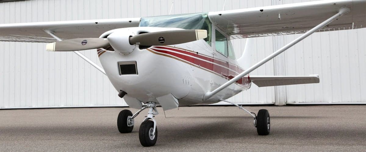 Front view of a Cessna aircraft with a white and red paint scheme parked in front of a hangar.