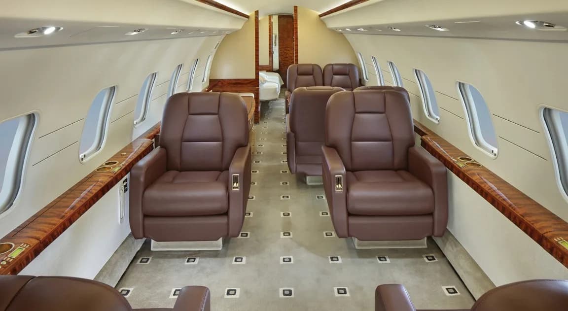 The interior of a Bombardier Challenger aircraft with leather seats and wood trim.