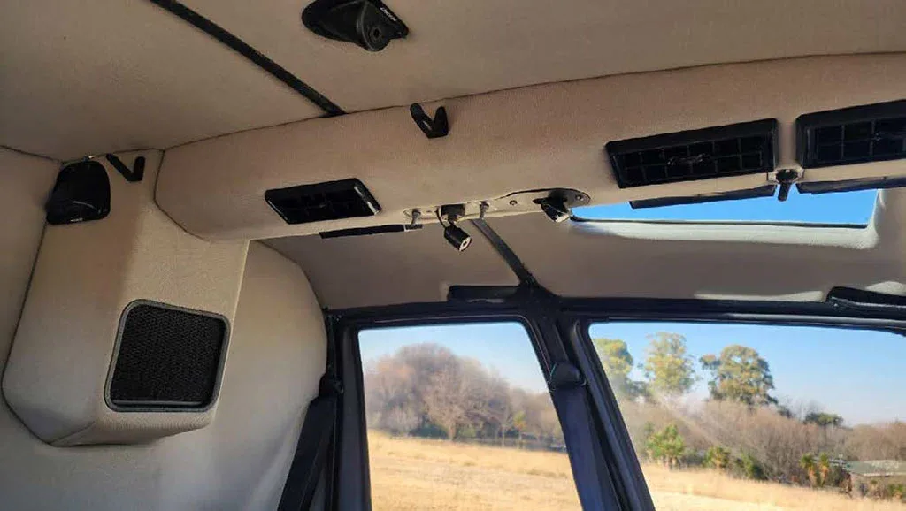 The beige ceiling and air vents of a helicopter cabin are shown, with a view of the exterior through the windows.