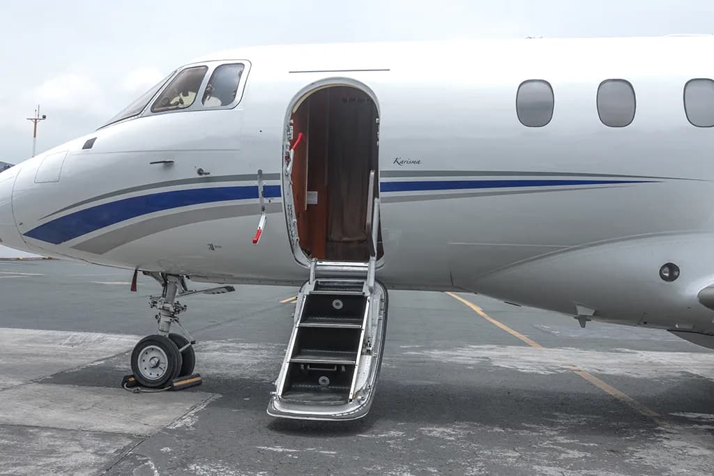 The front section of a white business jet with its main cabin door open and airstairs extended.