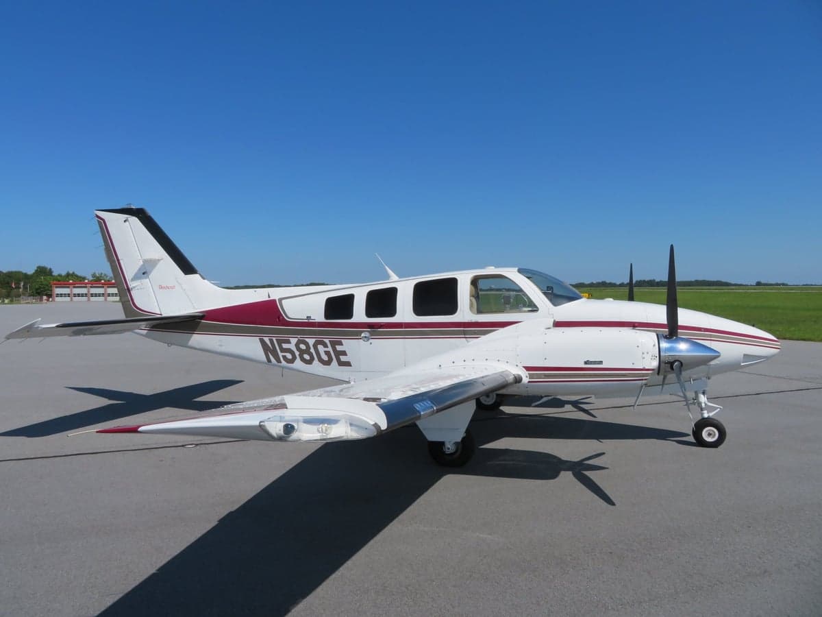 A Beechcraft Baron aircraft with a white and maroon paint scheme is parked on the tarmac.