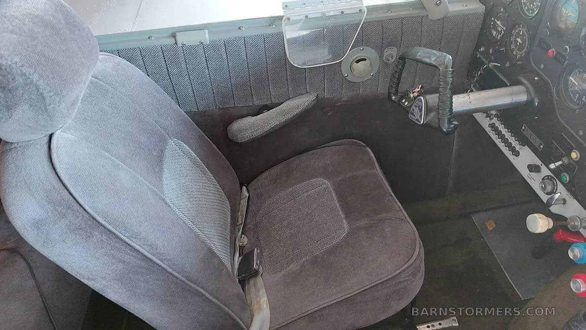 The gray fabric pilot's seat and side panel with controls inside a small aircraft cockpit.