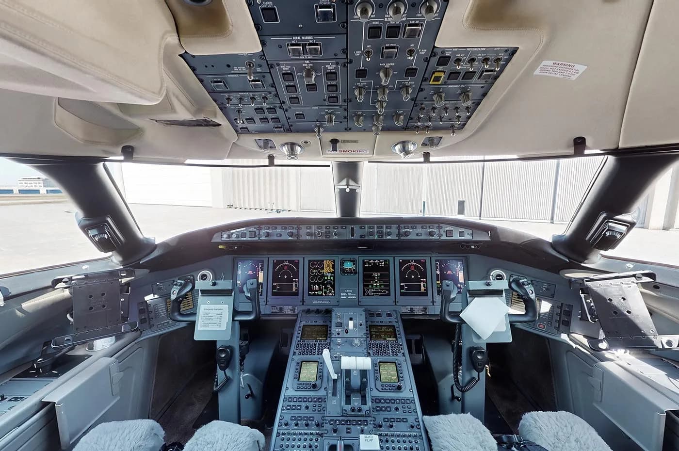 The modern cockpit of a private jet, featuring multiple digital displays, a complex control panel, and an overhead panel.
