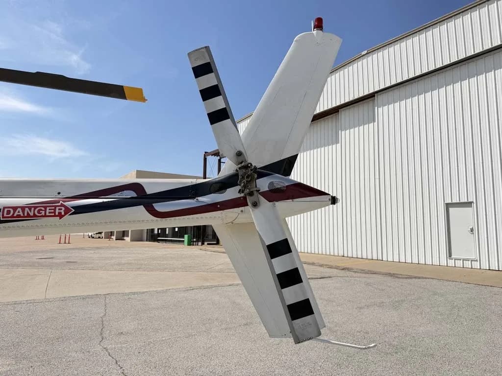 Close-up view of the tail rotor and vertical stabilizer of a white helicopter with black stripes.
