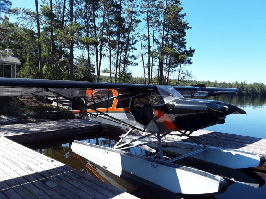 A black, gray, and orange Super Cub on floats is docked on a lake.