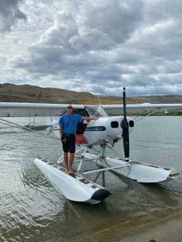 A man standing on the floats of a white and blue Super Cub floatplane.
