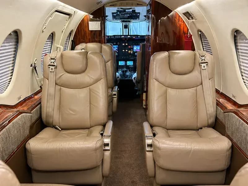 The aircraft's interior cabin features beige leather seats and wood paneling, looking towards the cockpit.