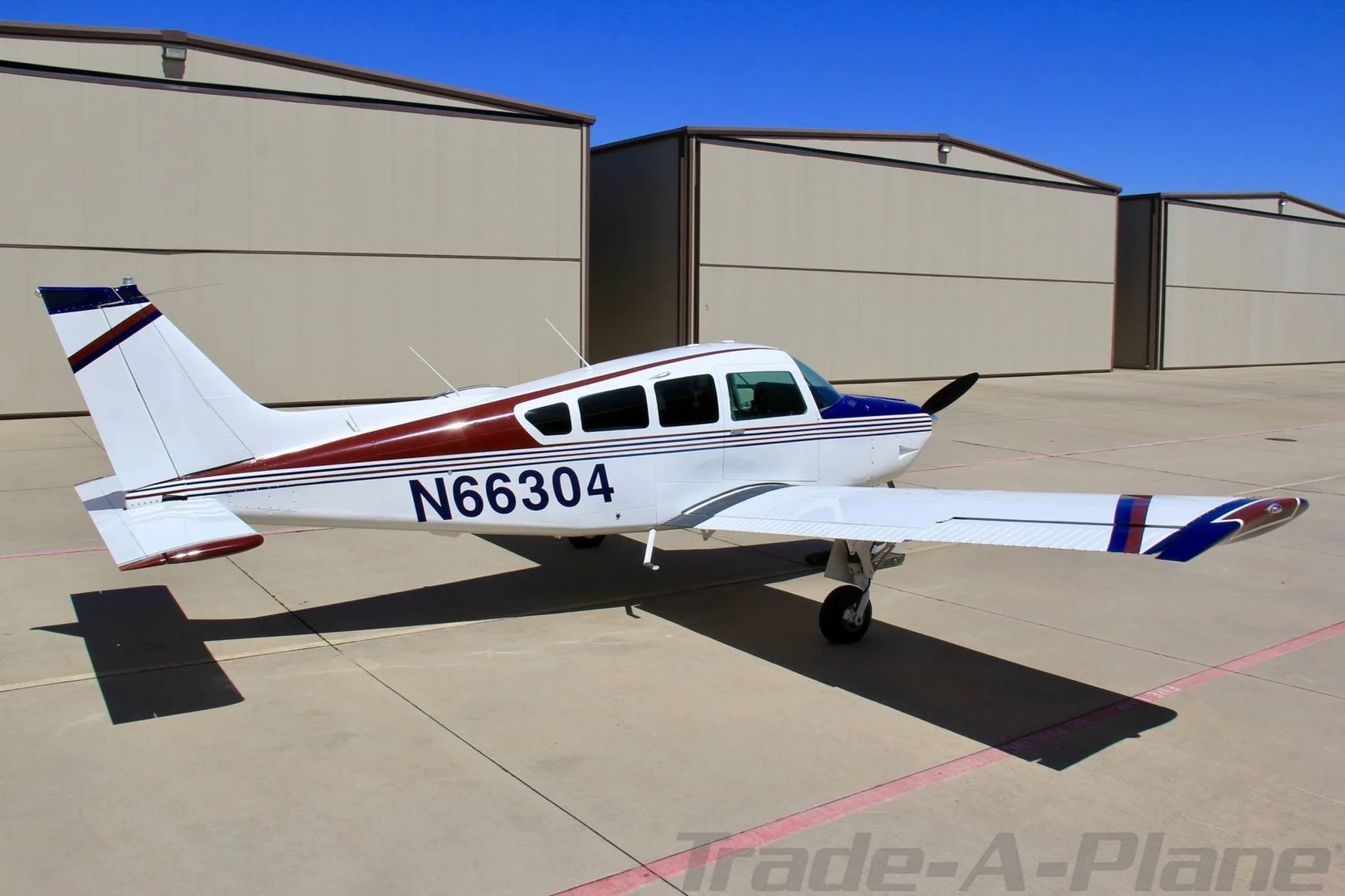 A three-quarter rear view of the white, blue, and red single-engine aircraft N66304 parked on an apron.