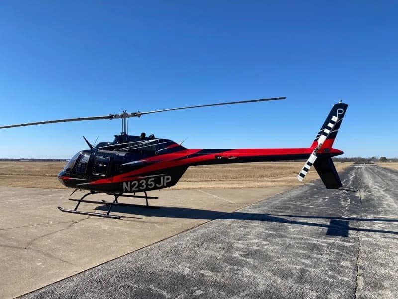Bell 206L-4 helicopter, registration N235JP, parked on a concrete pad with a black and red paint scheme.