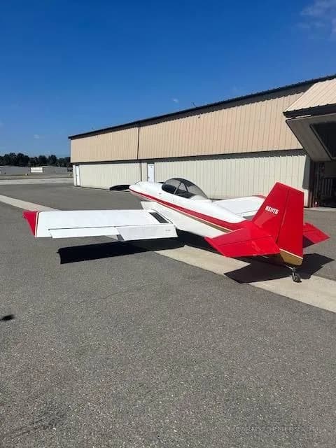 A white and red single-engine aircraft, possibly an experimental or aerobatic type, viewed from the rear-right, parked on an asphalt apron.