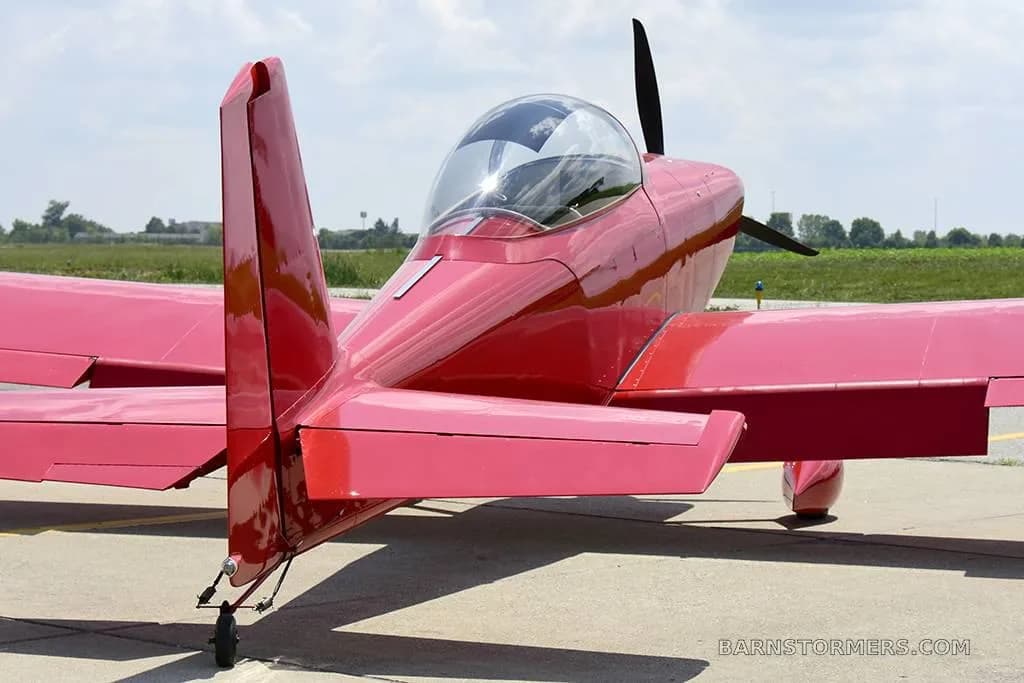 A rear view of a glossy red single-engine aircraft, showing its tail, horizontal stabilizers, and bubble canopy.