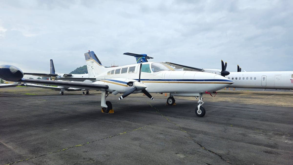 A white and blue Cessna aircraft parked on the tarmac with other aircraft in the background.