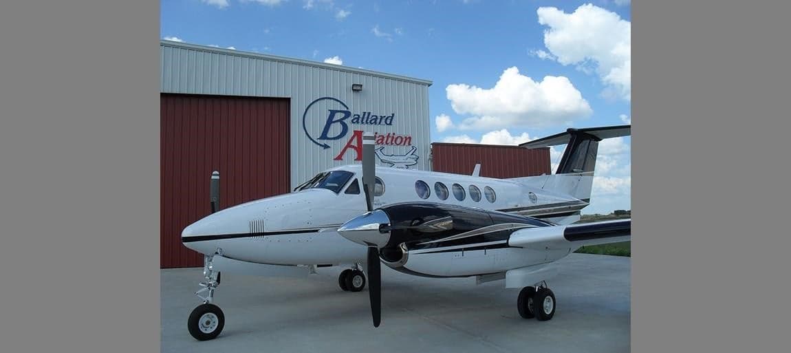 King Air aircraft parked in front of a hangar with the Ballard Aviation logo.