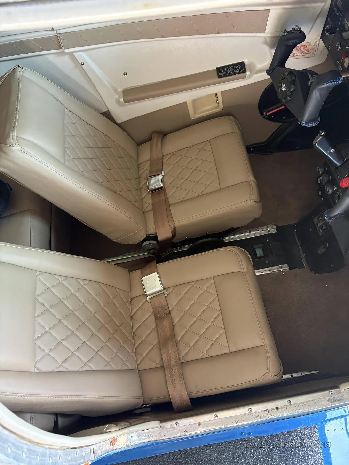 The tan leather interior of an aircraft cabin, showing two front seats with diamond stitching and seatbelts.