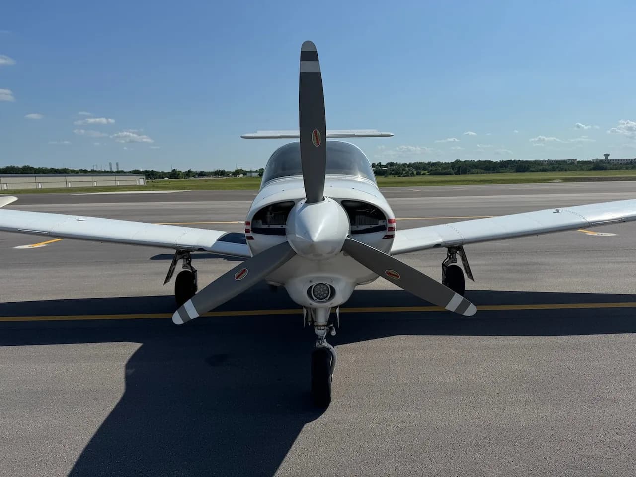 A white Piper Arrow II aircraft with red and brown stripes viewed head-on from the front on an asphalt tarmac.