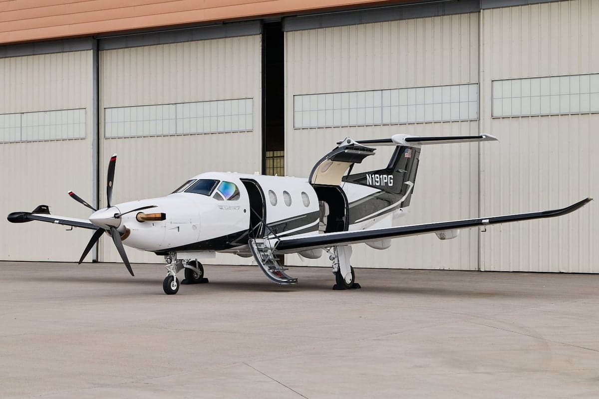 A white and black Pilatus PC-12 aircraft with tail number N191PG is parked on an airfield with its main door open and stairs extended.