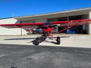 A red aircraft is parked in front of a building.