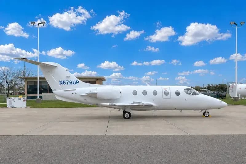 A white private jet, N676UP, is parked on an airport tarmac under a blue sky with white clouds.