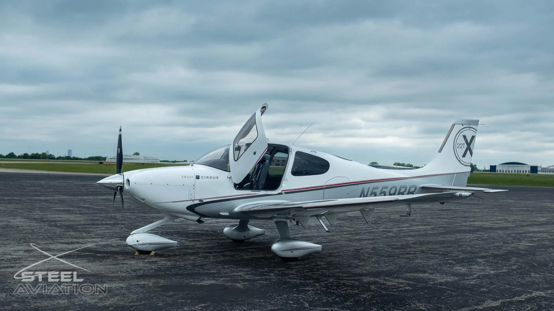 A white and silver Cirrus SR22T aircraft with registration N559RR has its gull-wing doors open on an airfield.