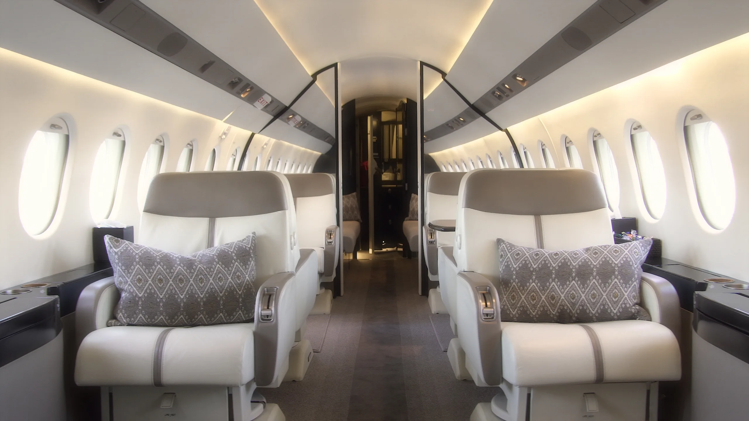 The luxurious cabin interior of a business jet with light-colored seats and a central aisle.