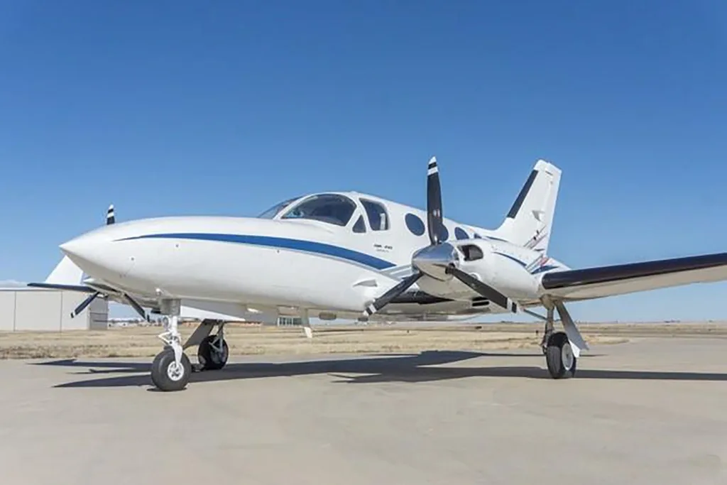 A white twin-engine Cessna 414 Chancellor aircraft with blue stripes on an airfield.
