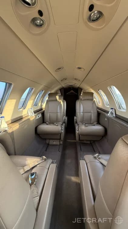 The interior cabin of a private jet with light brown leather seats facing each other.