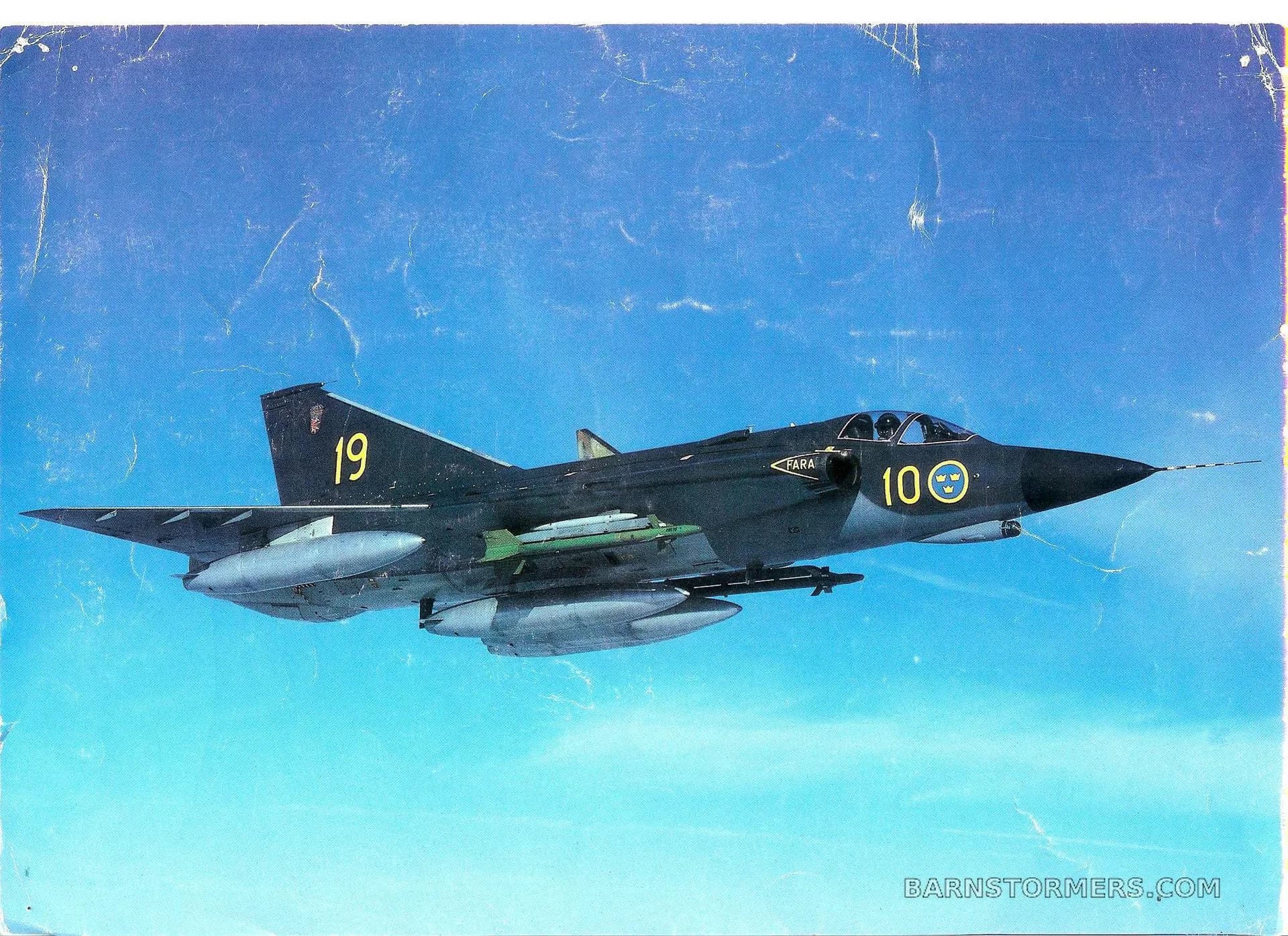 A dark green Saab J35 Draken fighter jet with '19' on its tail and '100' on its nose flies against a blue sky.