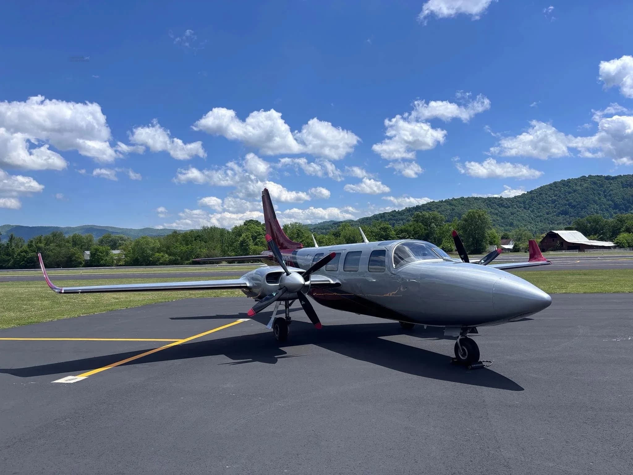 A front three-quarter view of a silver and red twin-engine Aerostar aircraft (N702PG) on an airfield.