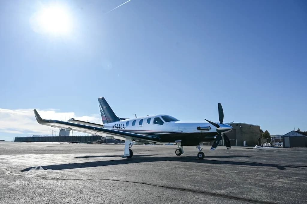 A TBM 940 aircraft, registration N944EA, parked on an asphalt ramp under a bright sunny sky.