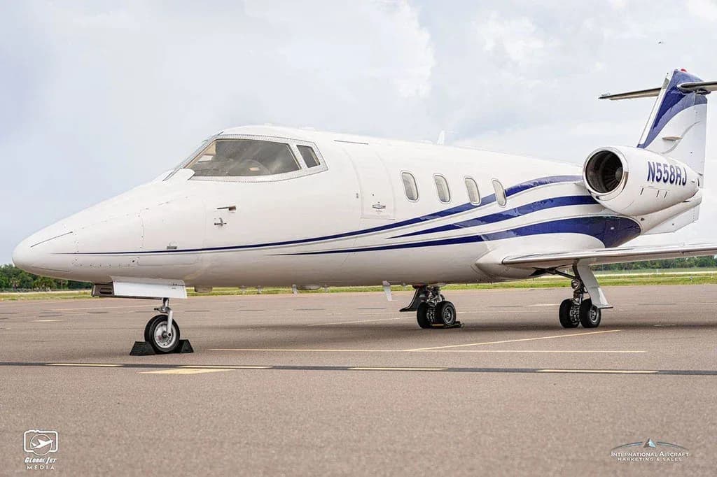 A close-up side view of the front section of a white business jet with blue stripes, tail number N558RJ, on an airfield.