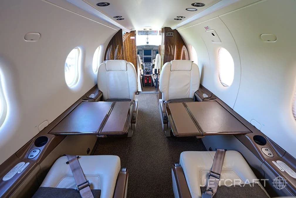 The aircraft cabin interior with light cream seats and fold-out tables, looking forward towards the cockpit.