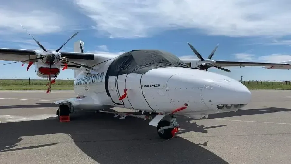 A white Let L-410 Turbolet aircraft is parked on the tarmac with a cover over the cockpit.