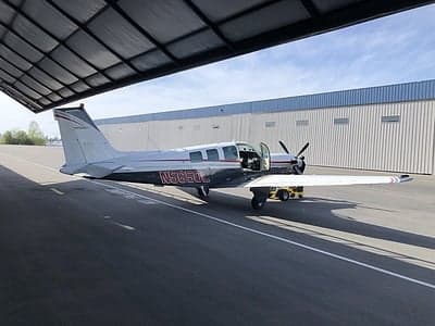 Side view of a Beechcraft Bonanza with the door open in front of a hangar.
