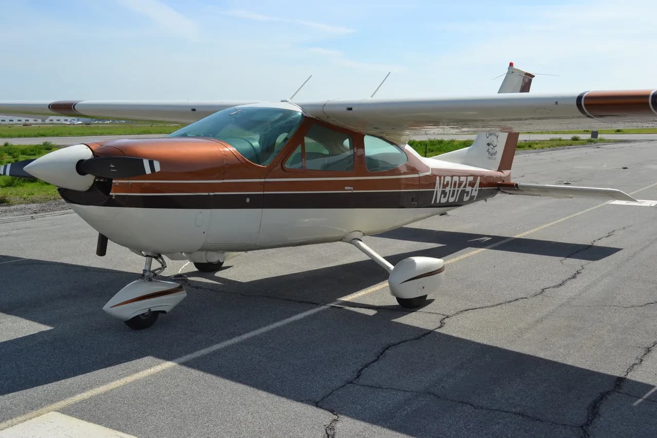 A brown and white single-engine, high-wing aircraft (N30754) is parked on an asphalt tarmac under a clear sky.