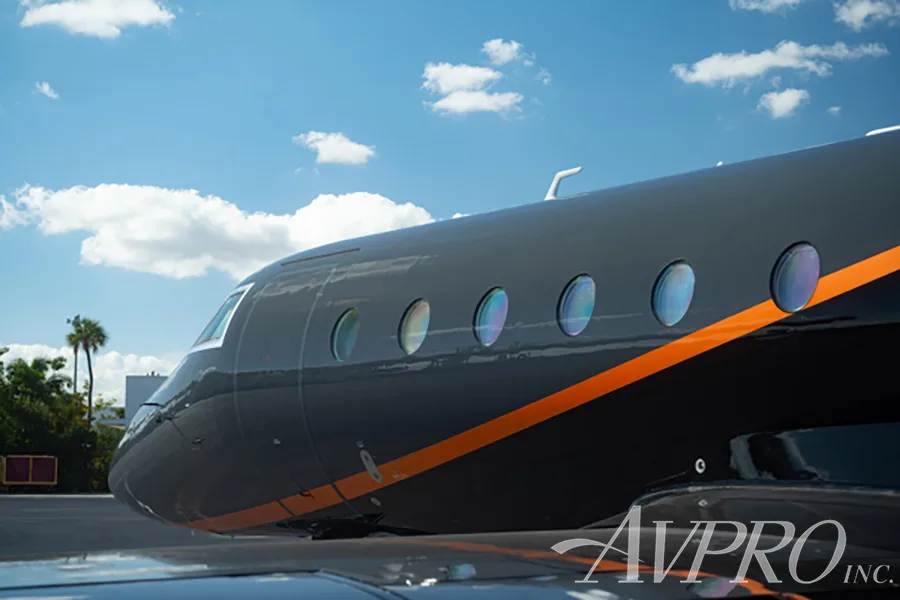 A close-up side view of the dark gray fuselage of the Gulfstream G200, showing the orange accent stripe and cabin windows.