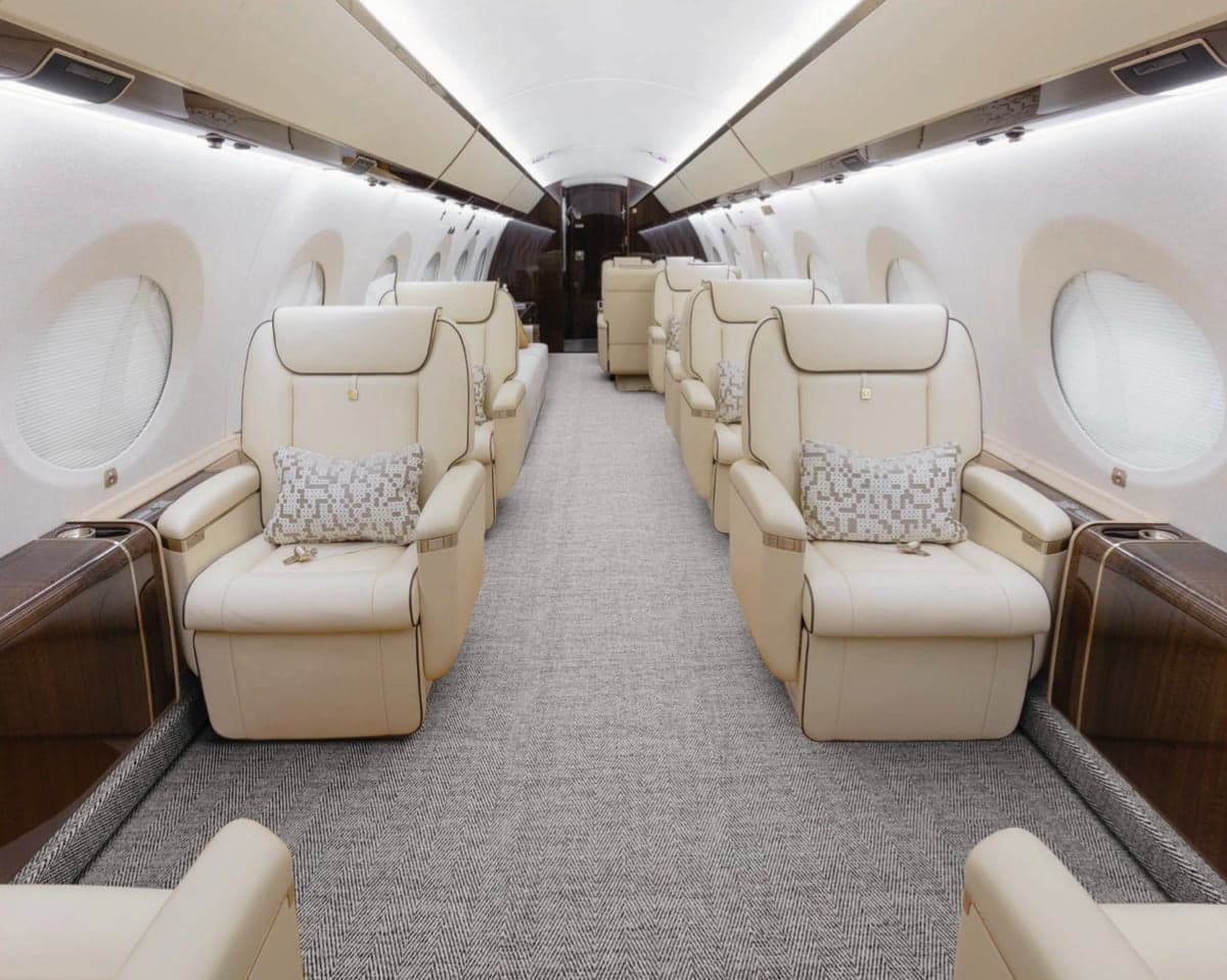 Aircraft cabin with cream-colored leather seats and gray carpet.