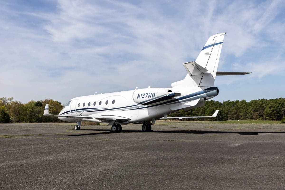 A white Gulfstream G150 aircraft with blue stripes, registration N137WB, is parked on the tarmac.