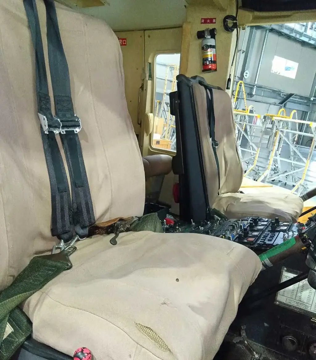 A view of the pilot's tan fabric seat and some controls in a helicopter cockpit.