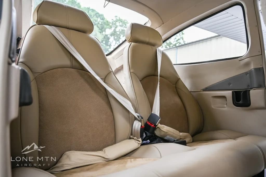 A side view of the tan leather rear seats with seatbelts in the aircraft cabin.