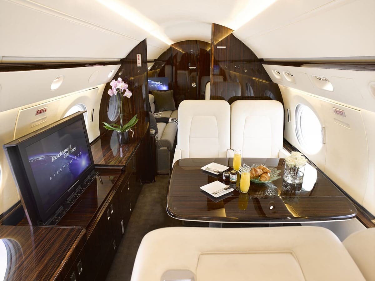 A view inside the Gulfstream G650 cabin, showing a dining table set with breakfast and a large entertainment screen.